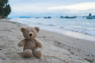 Teddy bear on shore by sea against sky during sunset