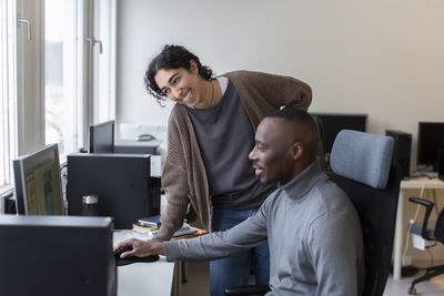 Businesswoman leaning at desk while discussing with male colleague in office