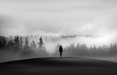 Silhouette man standing on field against forest during foggy weather
