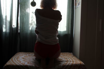 Rear view of woman standing by window at home