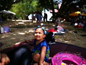 Cute girl looking at cropped person while sitting on picnic blanket at park