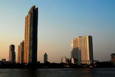 Skyscrapers by river against sky during sunset