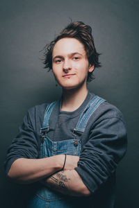 Portrait of trendy young man standing arms crossed over gray background