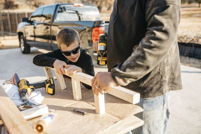 Midsection of father with son drilling wood while standing outdoors