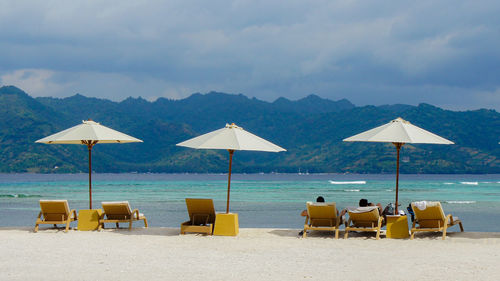 Lounge chairs and parasols on beach against sky