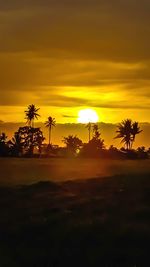 Scenic view of silhouette palm trees against orange sky