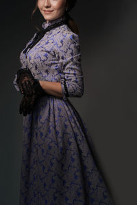 A girl standing in a blue dress in the style of the 1900s, in a retro dress on  a gray background.