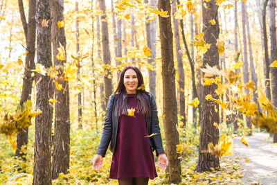 Portrait of smiling young woman standing in forest during autumn