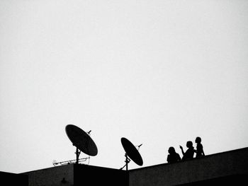 Low angle view of silhouette people on building terrace against clear sky