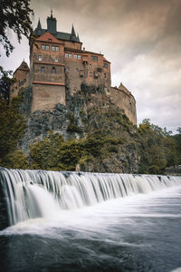 Scenic view of waterfall by building against sky