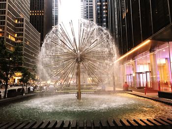 Illuminated fountain by building in city at night