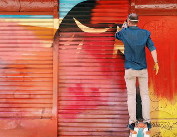 Rear view of man standing against graffiti wall