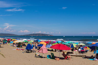 People and parasols at beach against sky