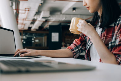 Midsection of woman using mobile phone while sitting on table