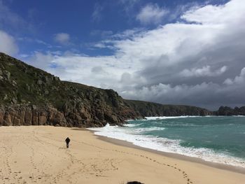 Man walking on sand at beach against cloudy sky