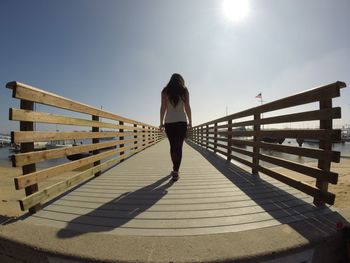 Rear view of woman standing on footbridge against sky