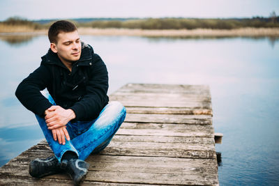 Man sitting on pier over lake against sky