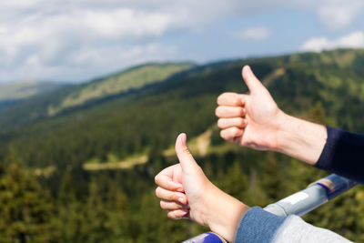 Cropped couple hands showing thumbs up by mountains