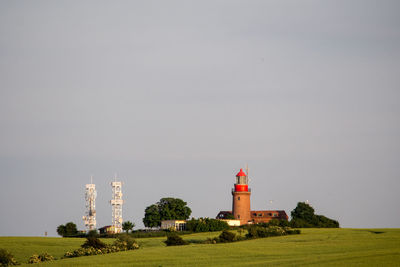 Lighthouse on field by building against clear sky