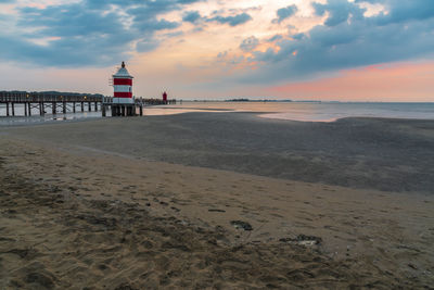 Lighthouse on beach against sky during sunset