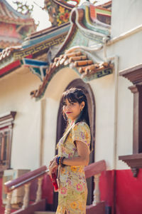 An asian woman in a yellow cheongsam qipao dress holding red fan standing in front of the gate