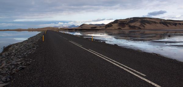 Road by lake and mountains against cloudy sky