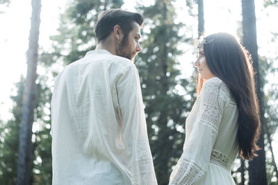 Side view of young couple standing against trees