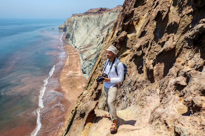 Man with camera on rock formation against sea and sky