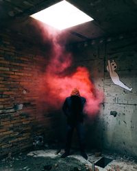 Hooded person by red smoke in abandoned building