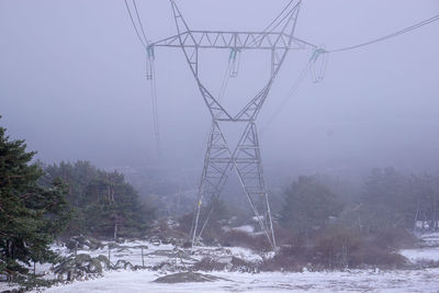 Electricity pylon on snow covered land against sky