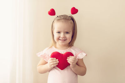 Portrait of girl holding heart shape against beige background