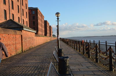 Empty footpath by sea against sky in city