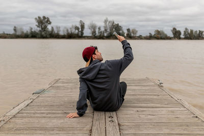 Rear view of man sitting on pier over lake