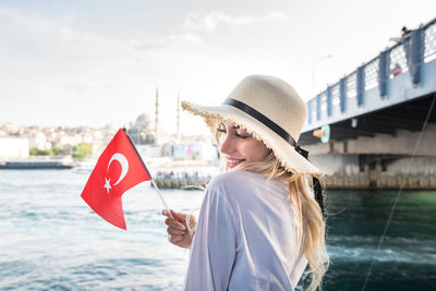 Young woman with umbrella standing against bridge over water