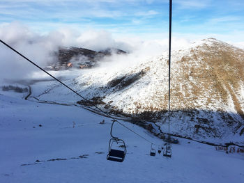 Ski lift over snow covered mountains against sky