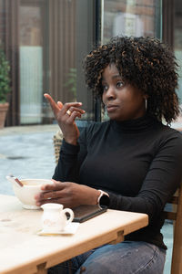 African american woman in red coat talking on smartphone near brick wall