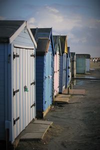 Beach huts on sand against cloudy sky