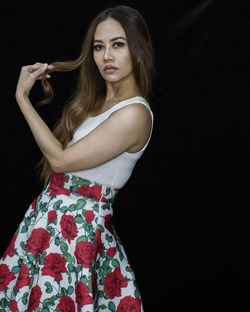 Portrait of young woman standing against black background