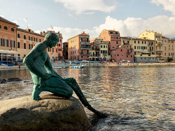 Statue by canal in city against sky