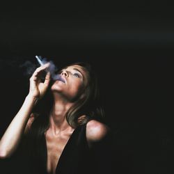 Young woman smoking against black background