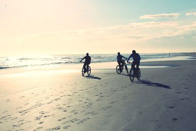 Friends riding bicycles at beach against sky
