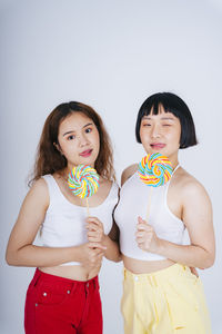 Portrait of lesbian couple holding lollipop against white background