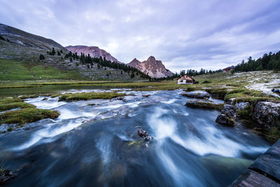 River flowing through rocks against cloudy sky