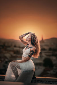 Side view of woman standing by sea against sky during sunset