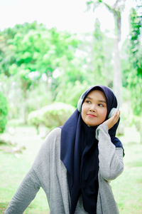 Portrait of young woman standing against trees