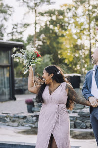 Cheerful young bride holding bouquet walking with groom at wedding