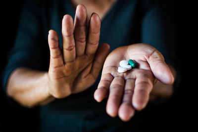 Close-up midsection of woman holding medicines against black background