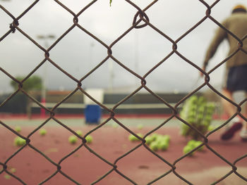 Rear view of man at tennis court seen through chainlink fence