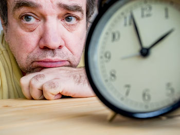 Close-up of clock against sad man in background on table
