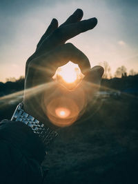 Close-up of hand holding sun against sky during sunset